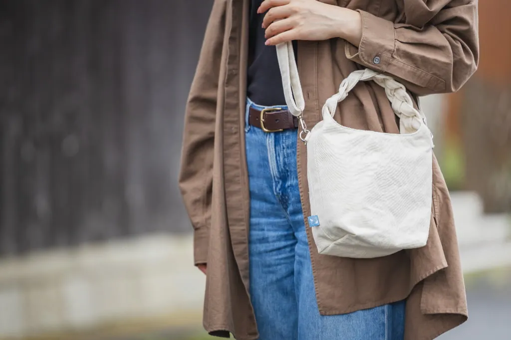 出典: サニーフォトグラフィー, ライセンス: サイト内利用規約に基づく引用。代替: https://web.archive.org/web/*/https://sunnyphoto.net/works/detail/nunonishitai 三つ編みバッグの使用シーン、女性が持つ様子