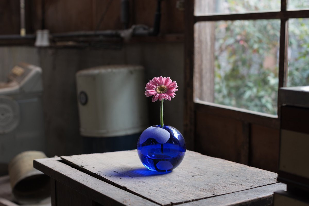 琵琶湖の古民家台所に置かれた青い地球型花瓶にピンクの花が挿された新作「あいまいな地球に花束を」。世界中の人々が描いた曖昧な世界地図を基にしたキュンチョメの立体作品。