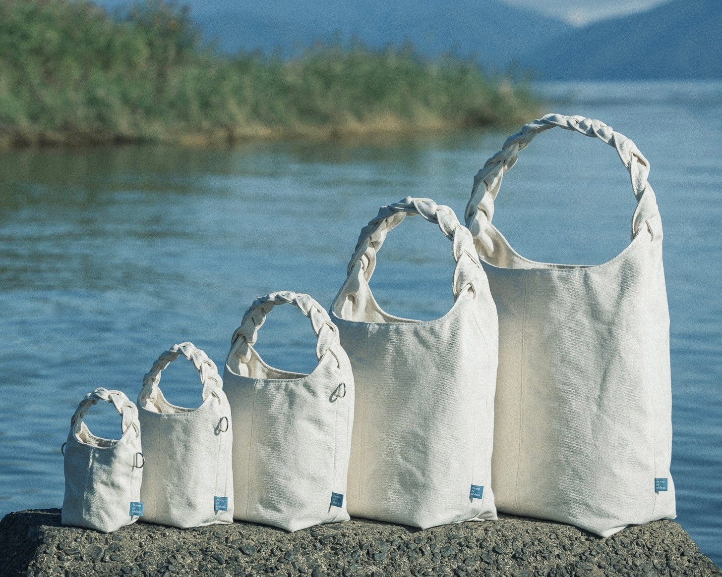 PR TIMESのプレスリリース掲載画像。三つ編みバッグ既存モデルの製品写真で、持ち手の編み込みと本体の布地がクローズアップされ、ブランドが磨いてきた基本形の質感を示す。