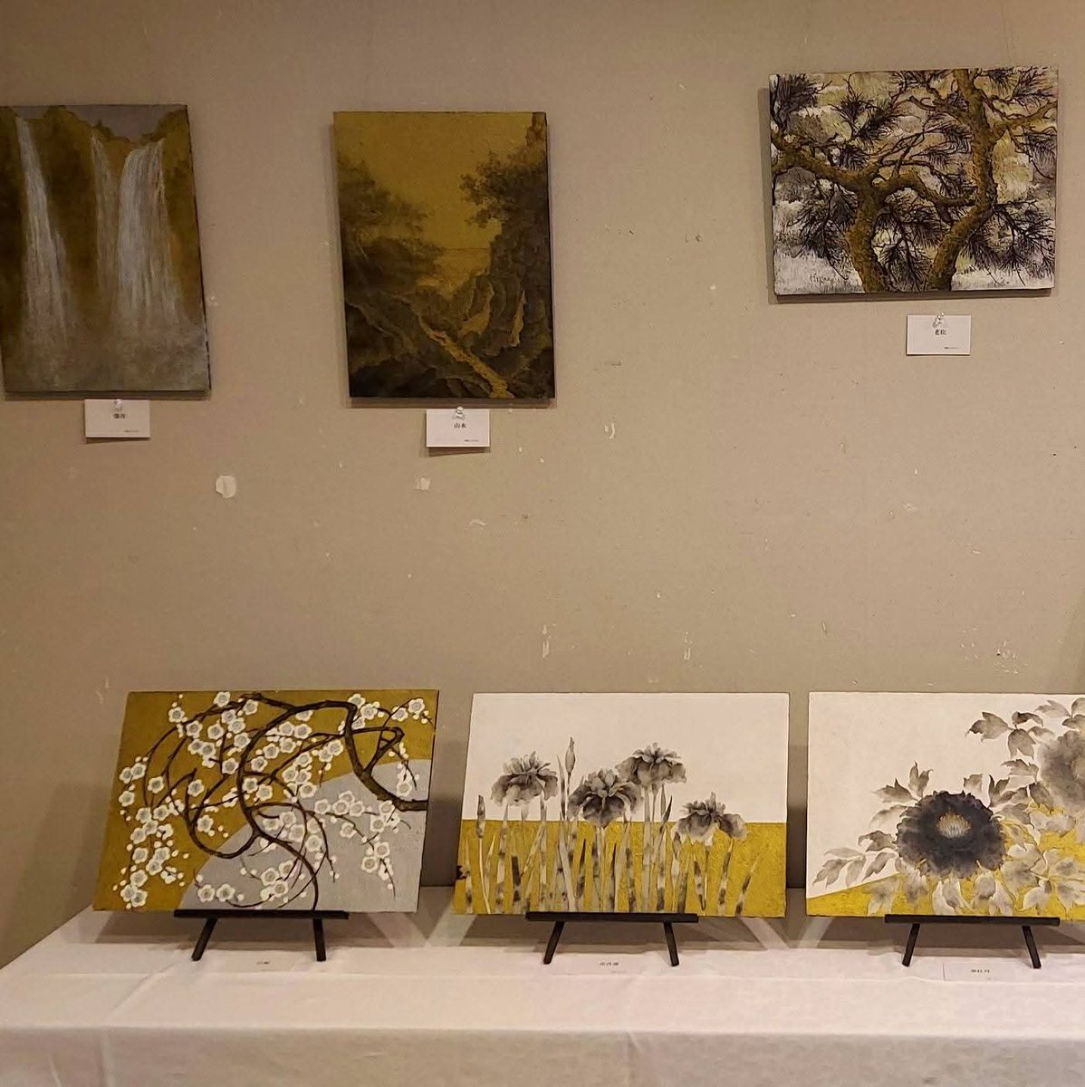 今津サンブリッジホテル1階ロビーギャラリーの展示風景。壁面の滝・渓流・老松を題材にしたアートパネルと、テーブル上の花をモチーフにした染めパネルが、水辺の景観を静かに示している構図。