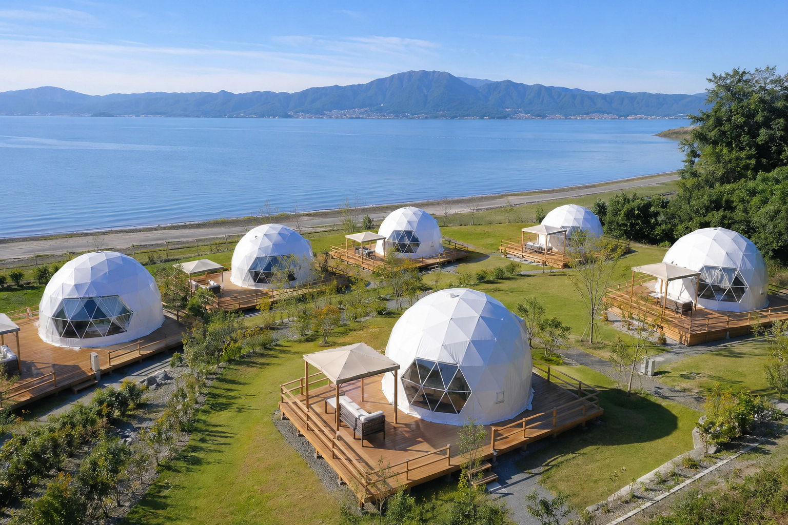 琵琶湖を望むグランドーム滋賀高島のドームテント群。昼間の開放的な外観で、プライベートデッキと湖畔のロケーションが明確に分かる施設全体の風景
