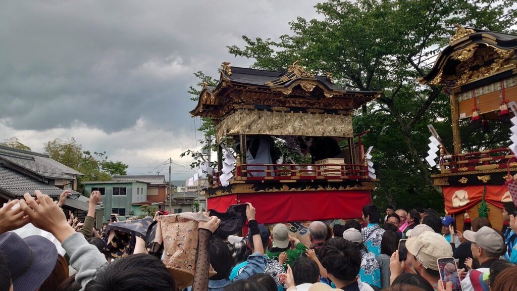 高島市大溝祭の本祭で曳山から参拝者に向かって盛大に餅をまく様子。多くの見物客が手を伸ばす賑わいある一場面で、400年続く伝統行事の活気を象徴。