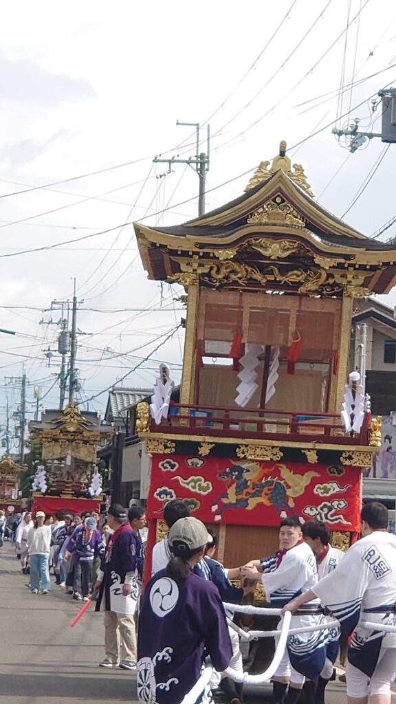 大溝祭で豪華に装飾された曳山を若衆が力強く曳く様子。朱と金の装飾が輝く伝統的な山車の迫力と、参加者の熱気が伝わる一枚。