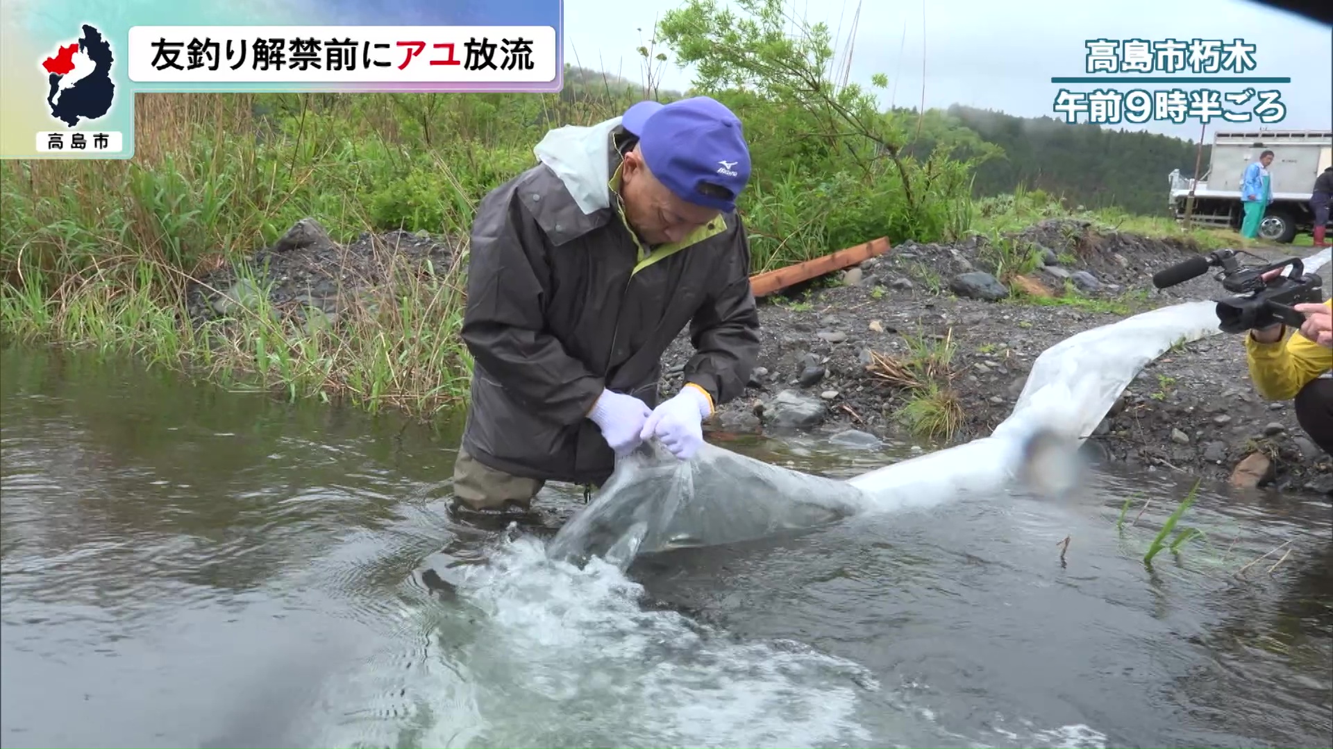 朽木漁協の関係者が川岸で放流作業にあたる様子。ホースや川岸の設備が写る報道写真。