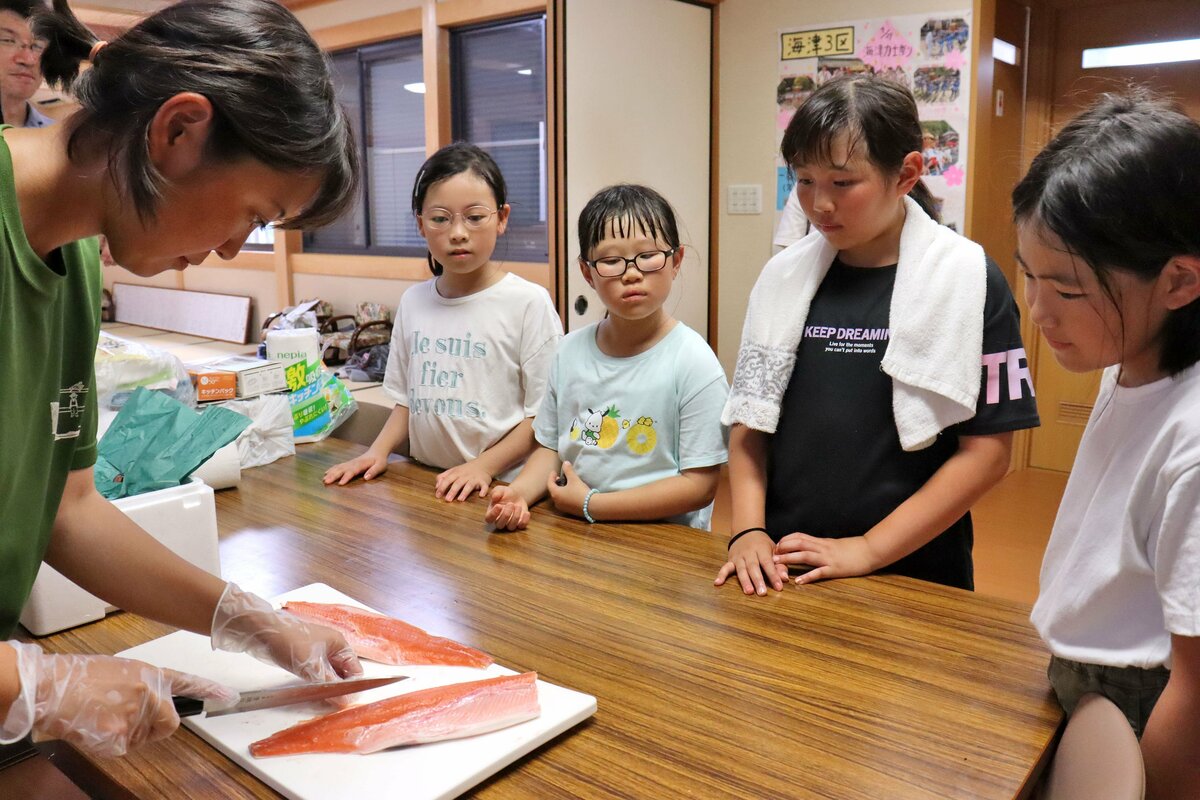 海津で魚をさばく女性漁師と、見る小学生